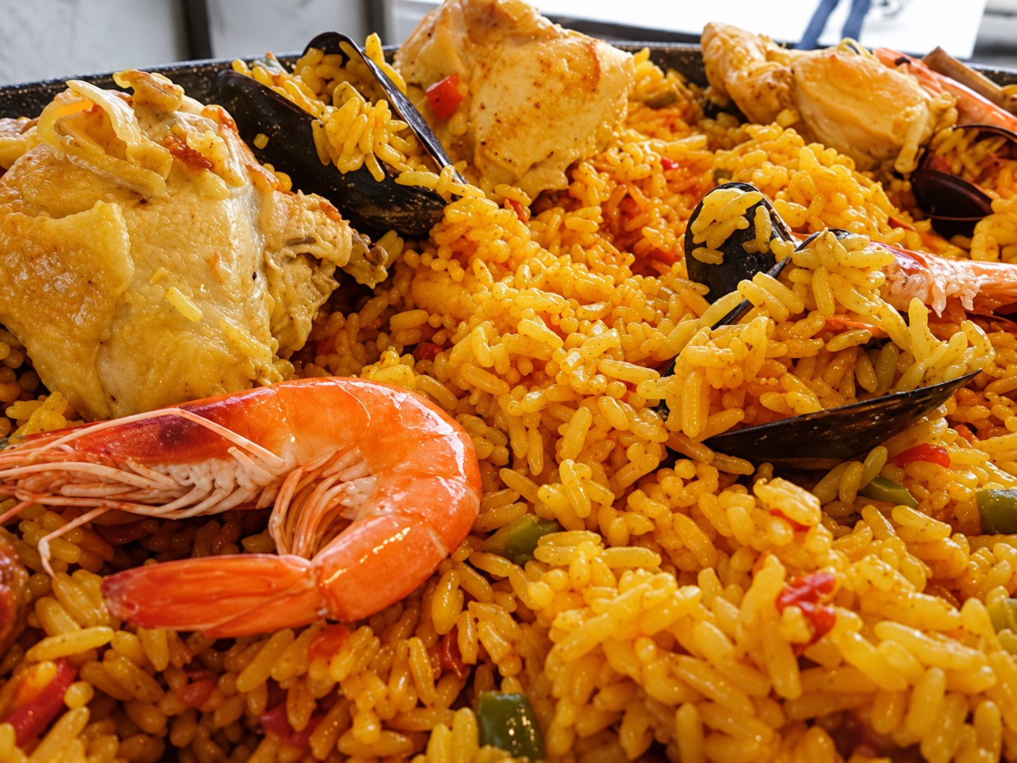 Gros plan sur une paella au riz jaune safrané garnie de crevettes, de moules et de morceaux de poulet.